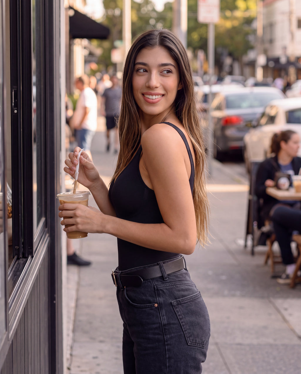 The Cooling Sculpt Bodysuit in Black styled with jeans at an outdoor cafe