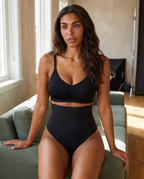 No-Show Tummy Control Thong in Black — seated on a green couch.