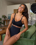 No-Show Tummy Control Thong in Black — on a green couch, laughing.